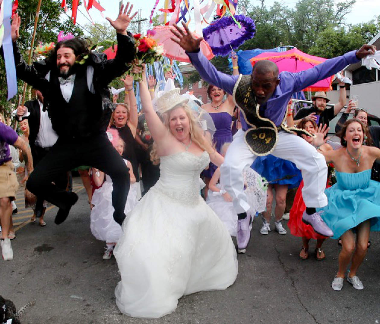 A wedding party leaping for joy in the street under colorful ribbons